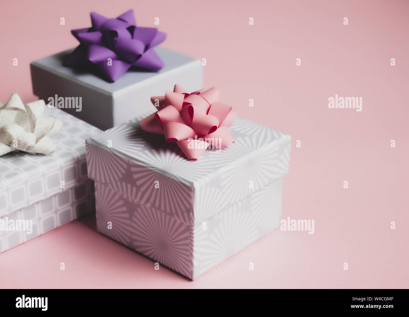 Three light gray gift boxes with colorful bows on pink background. Festive concept. Stock Photo
