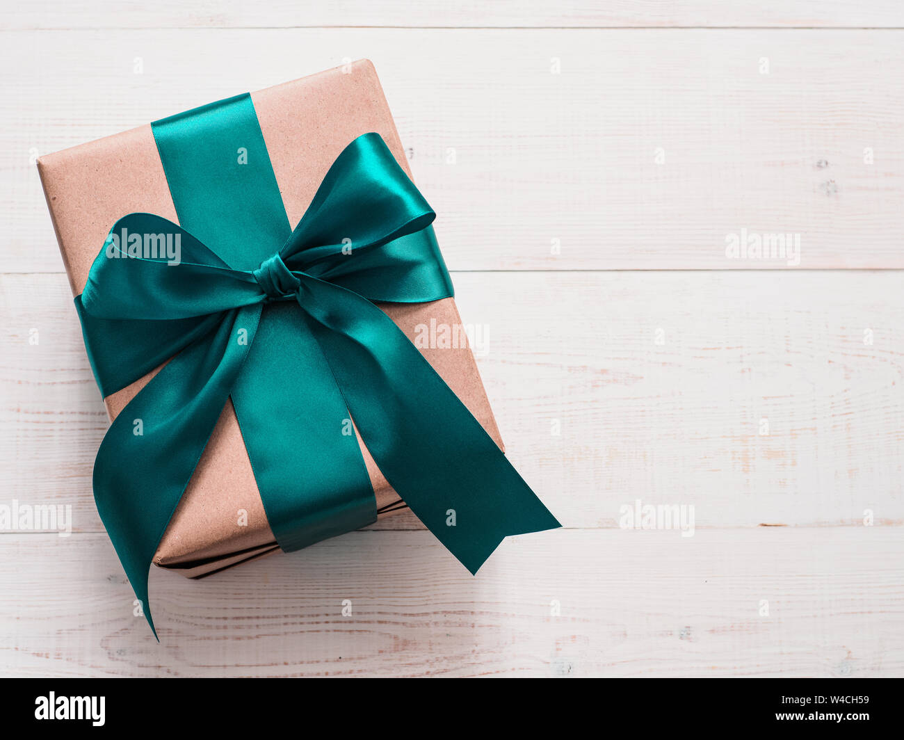 Gift box in craft wrapping paper and green satin ribbon on white
