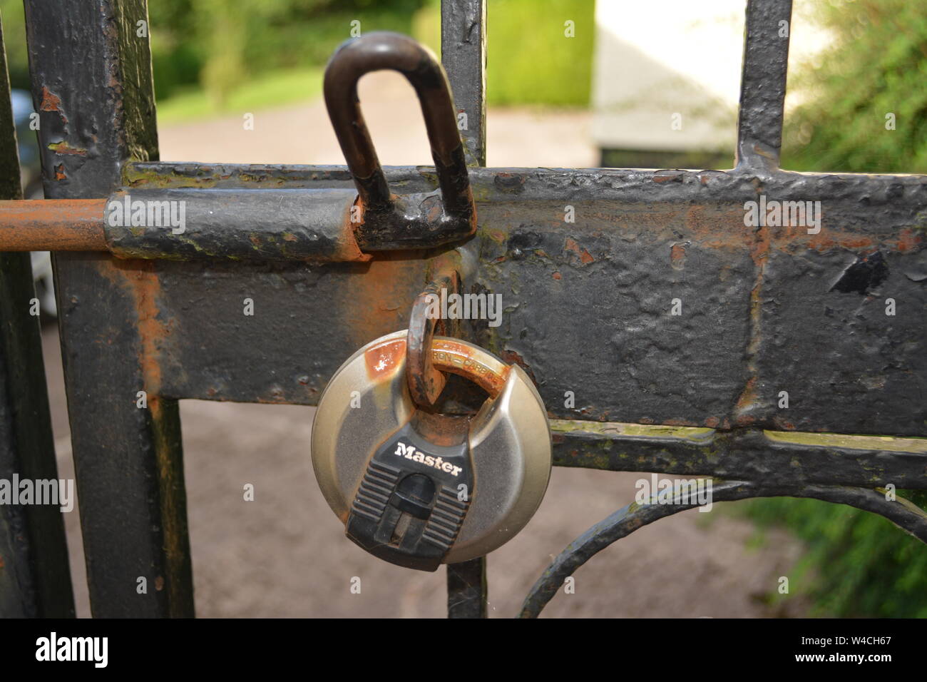 Circular Master security lock on black painted rusting wrought iron fence with open latch re home house security Stock Photo