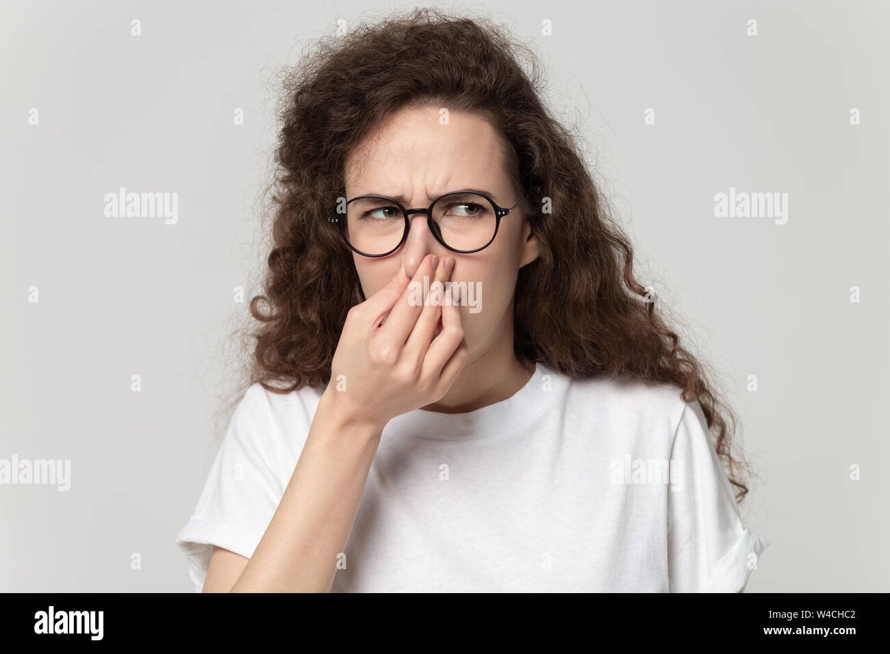 Headshot portrait girl plugs nose feels unpleasant smell studio shot Stock Photo