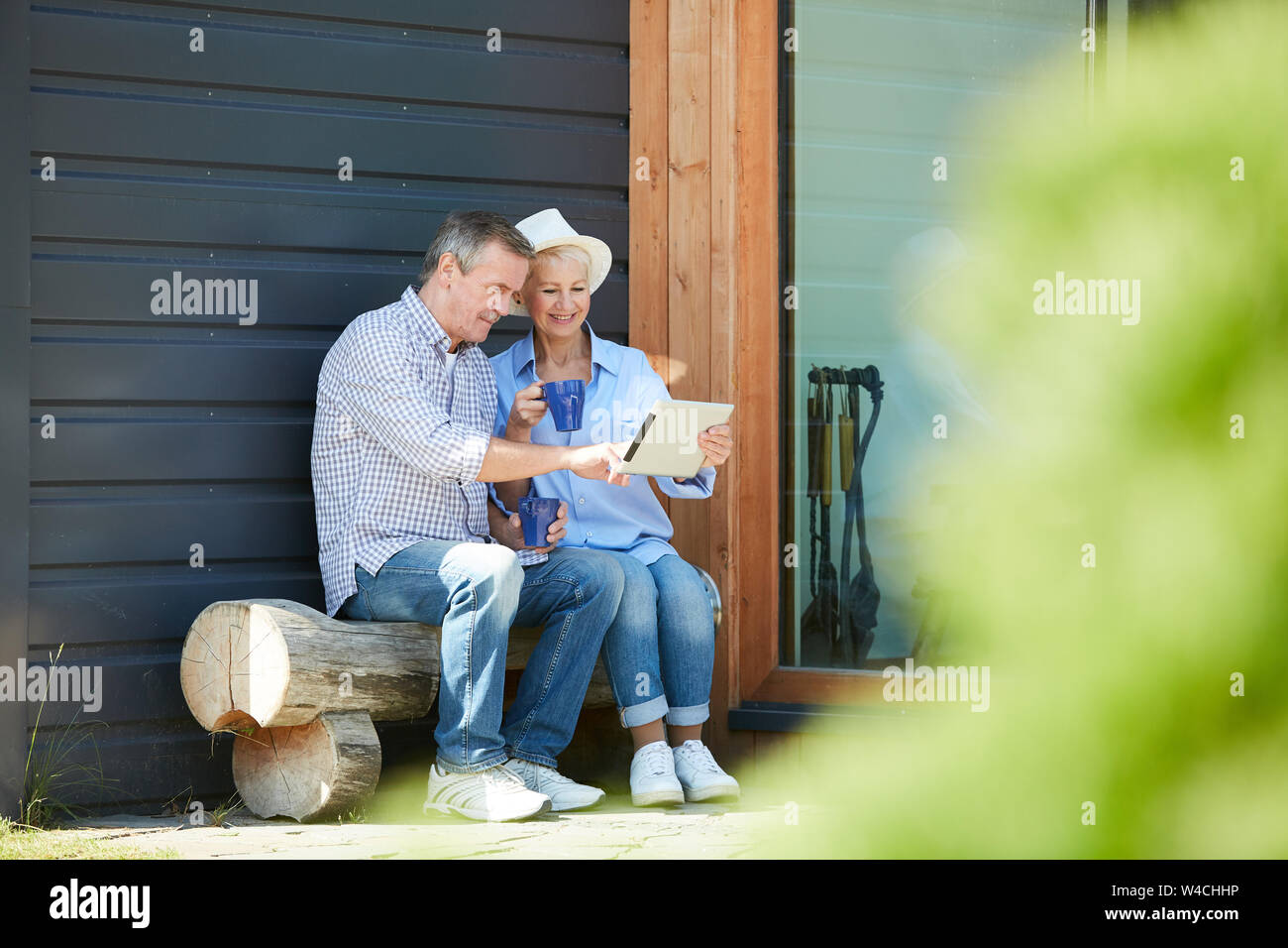 Full length portrait of contemporary mature couple using digital tablet while sitting in back yard outdoors, copy space Stock Photo