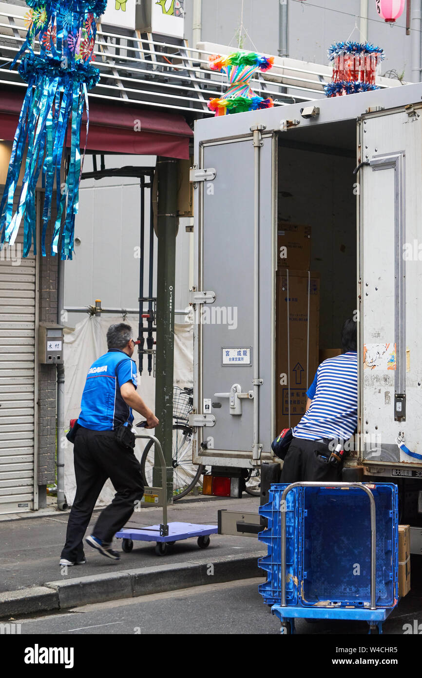 Two Japanese men working for Sagawa unload a delivery truck and push a luggage cart underneath