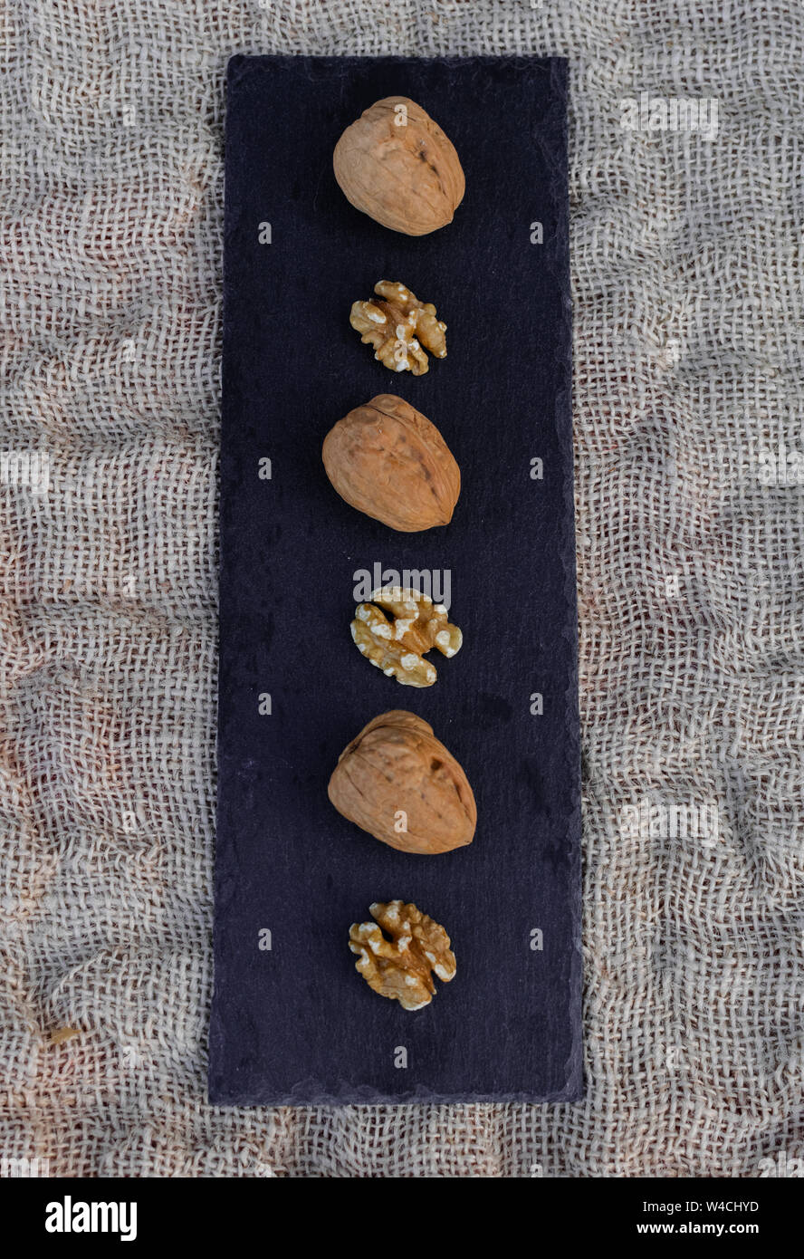 Walnuts, with and without shell, on black table surface, over sack texture Stock Photo