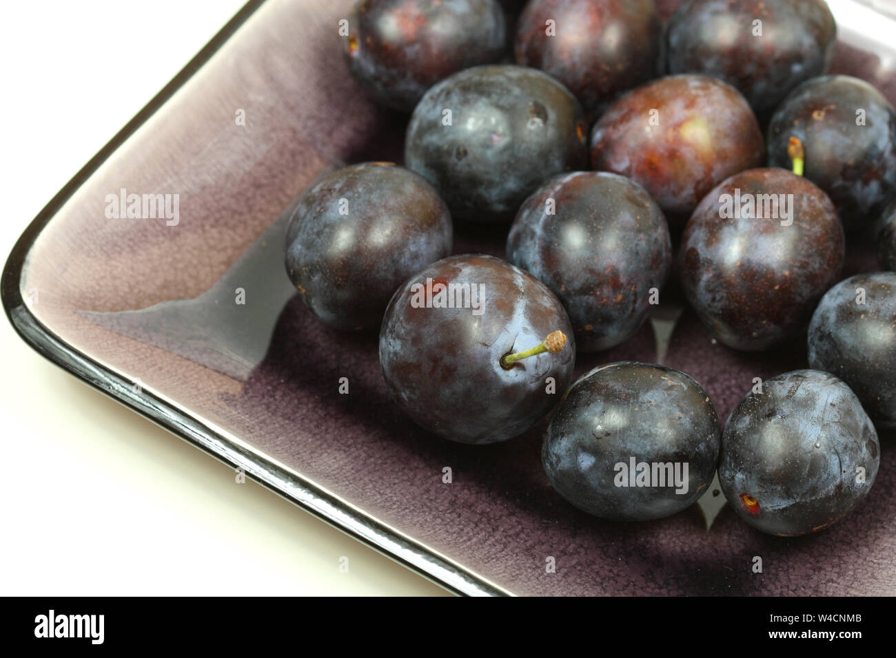 Plums on purple dish over white Stock Photo