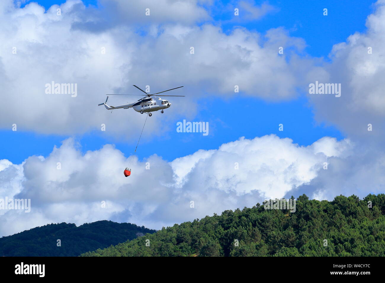Firefighting helicopter intervenes for the fire that starts on the forest-covered mountain. Stock Photo