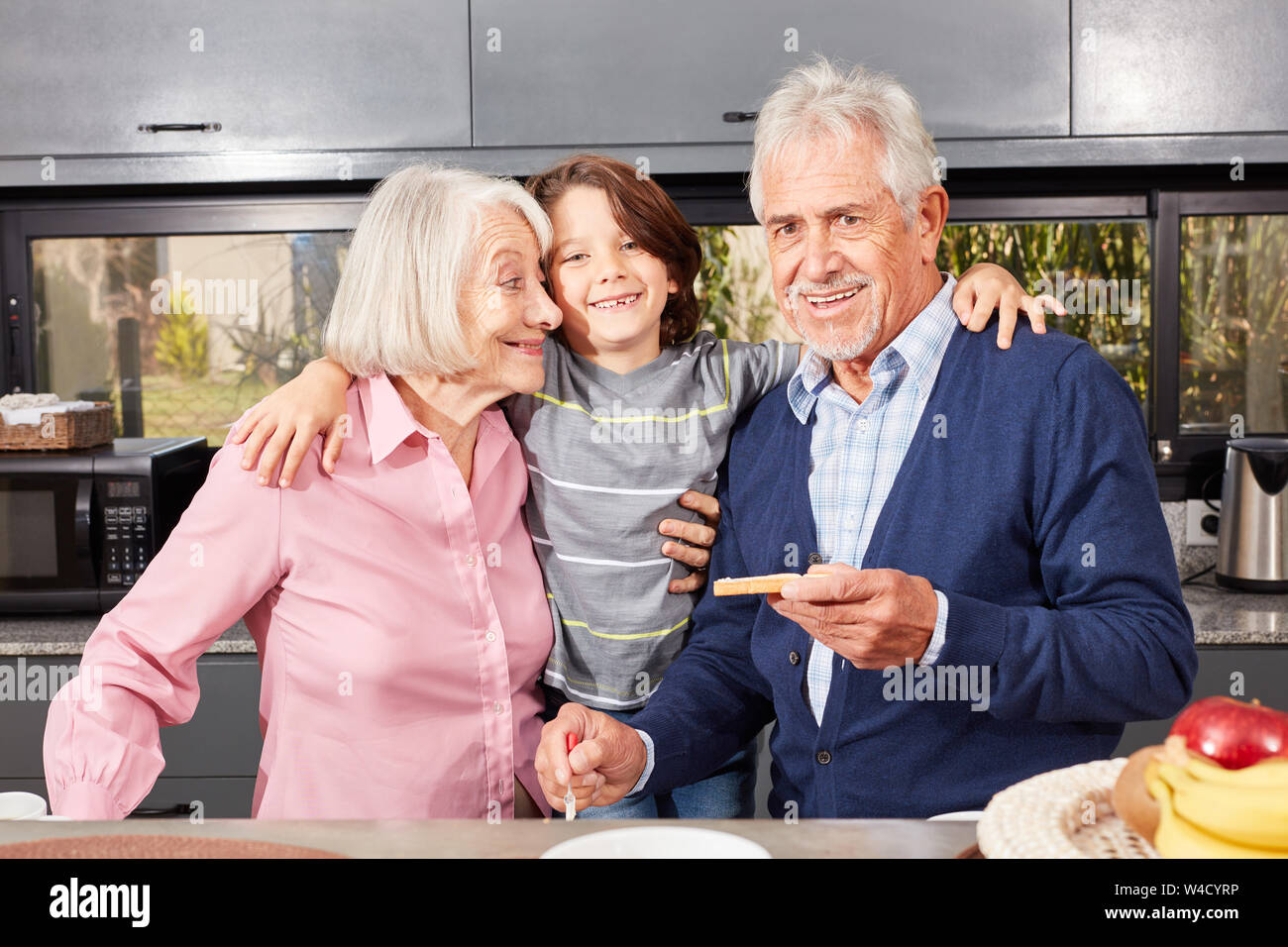 Happy grandson between granny and granddad in the morning in the kitchen having breakfast Stock Photo