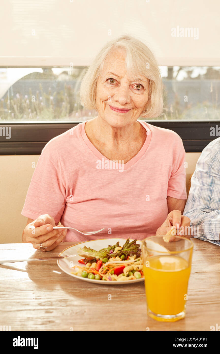 Senior eating healthy salad and drinking orange juice at lunch Stock Photo