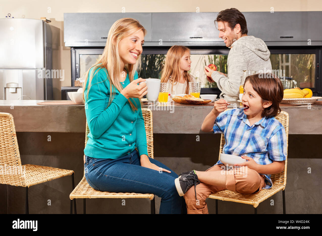 Mother and son have breakfast in the kitchen with father and sister in the background Stock Photo