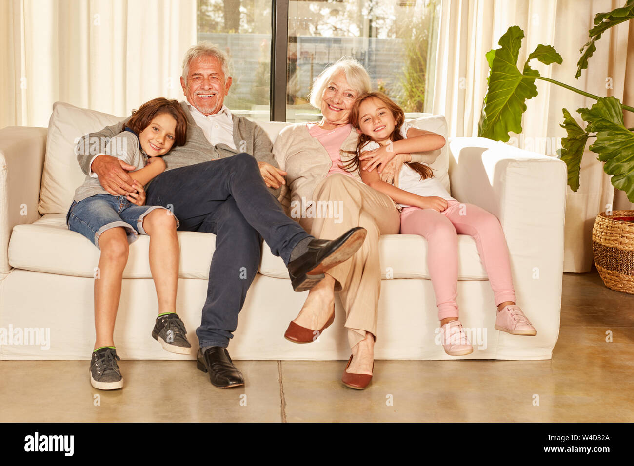 Happy grandparents and two grandchildren are sitting on a sofa in the apartment Stock Photo