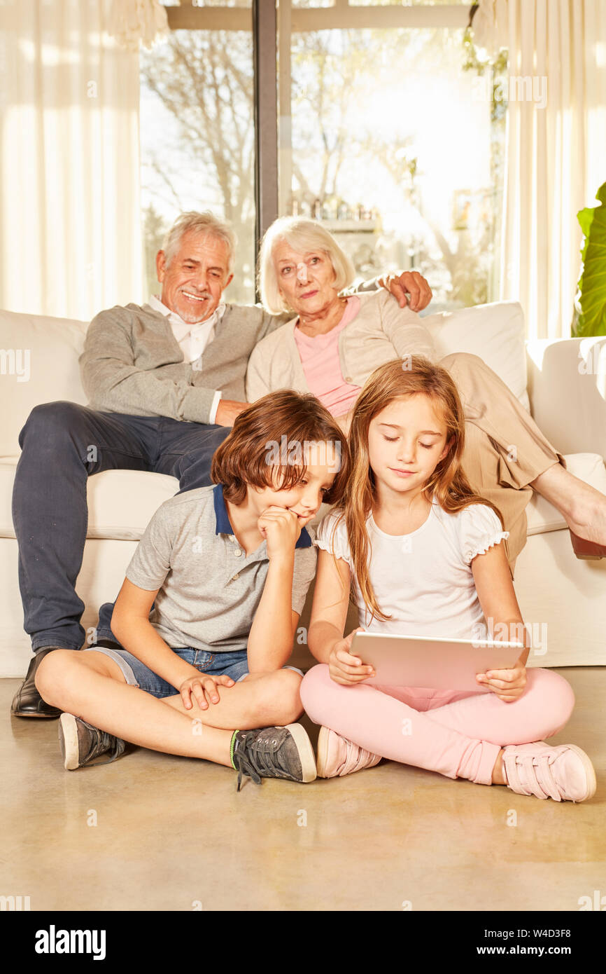 Grandchildren are surfing the internet using the tablet PC and grandparents are watching on the sofa Stock Photo