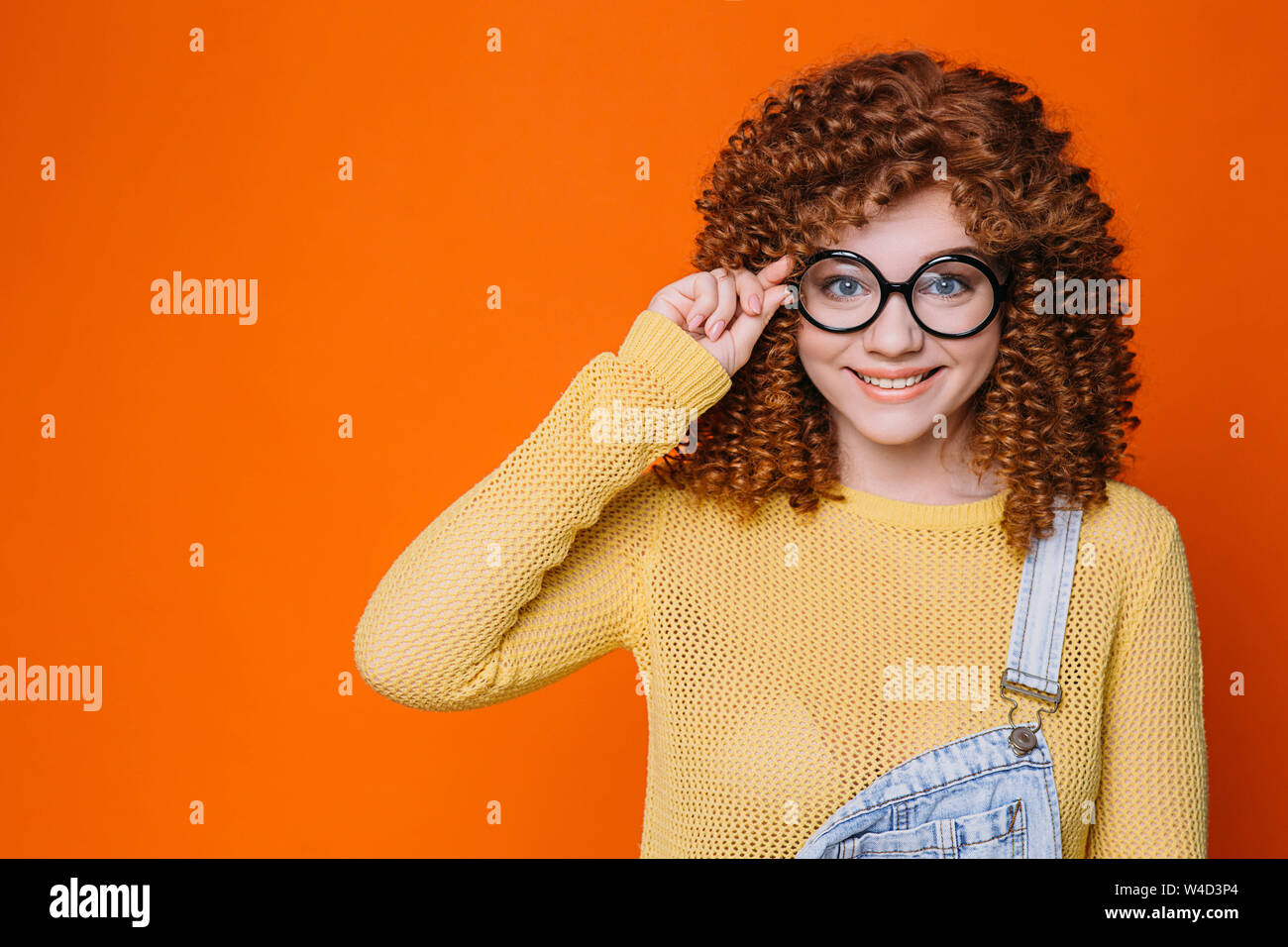 Student, curly haired hipster adjusting her eyeglasses and lookong at camera Stock Photo
