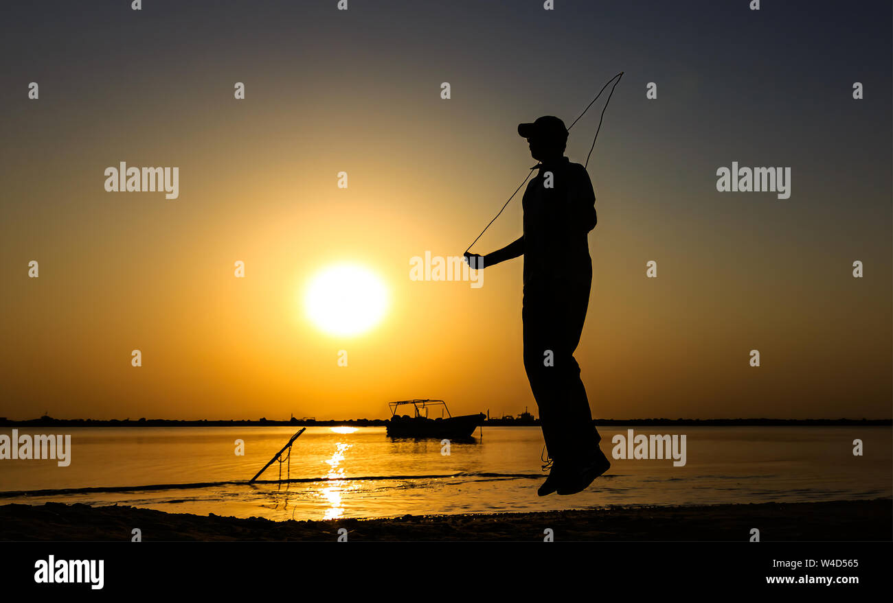 Young Man jumping rope at seaside. silhouetted Man rope skipping in sunset Stock Photo