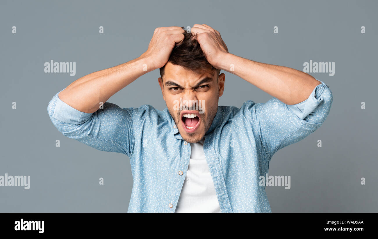 Frustrated Guy Pulling His Hair Out On Gray Studio Background Stock Photo