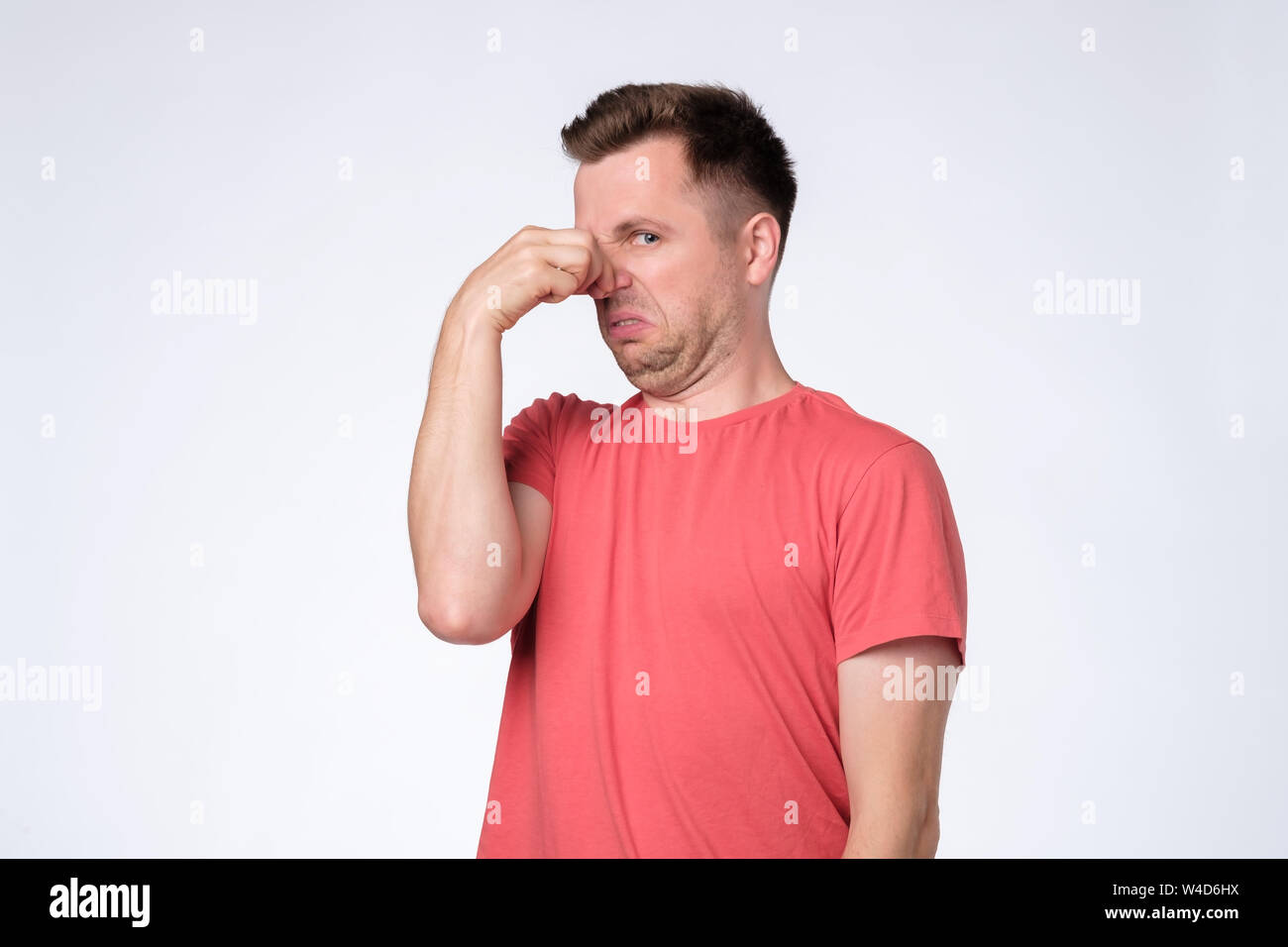 Displeased young man plugs nose as smells something stink and unpleasant. Stock Photo
