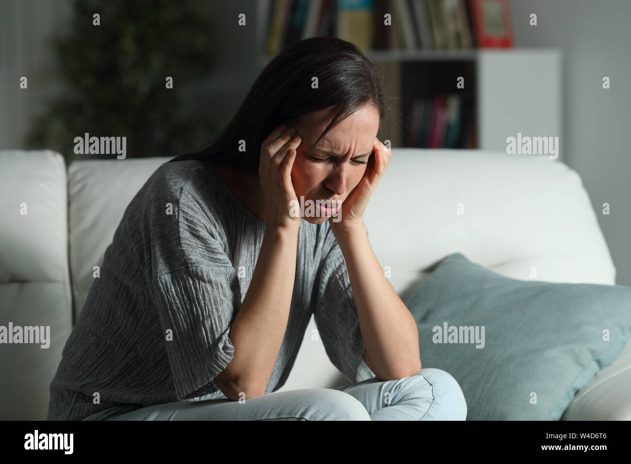 Woman suffering migraine in the night sitting on a couch in the living room at home Stock Photo