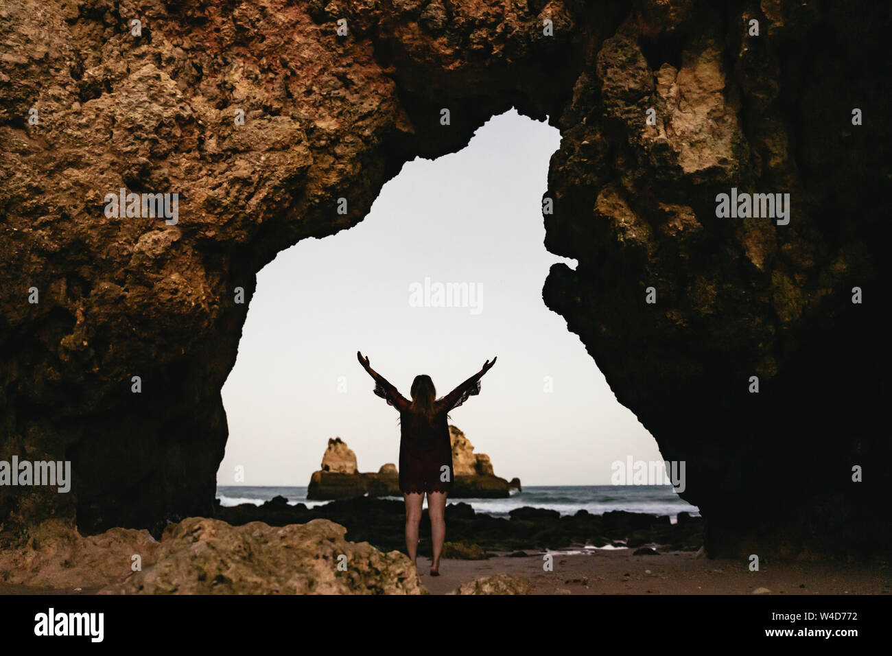 Young woman standing celebrating under a sea arch Stock Photo