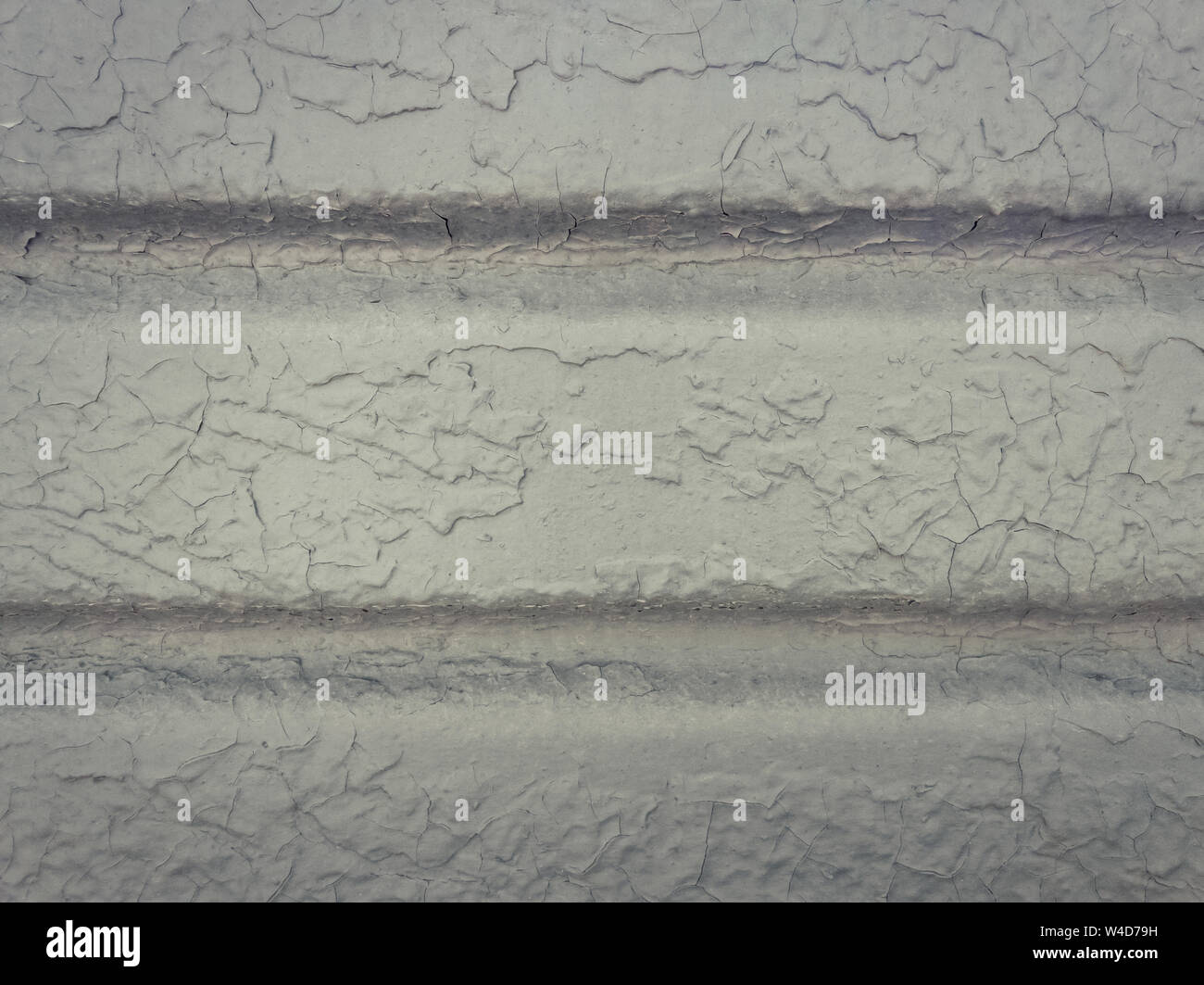 Grey paint peeling off a metallic surface background. Old grungy, weathered painted wall texture. Cracked, dirty, silver plaster falling off the const Stock Photo