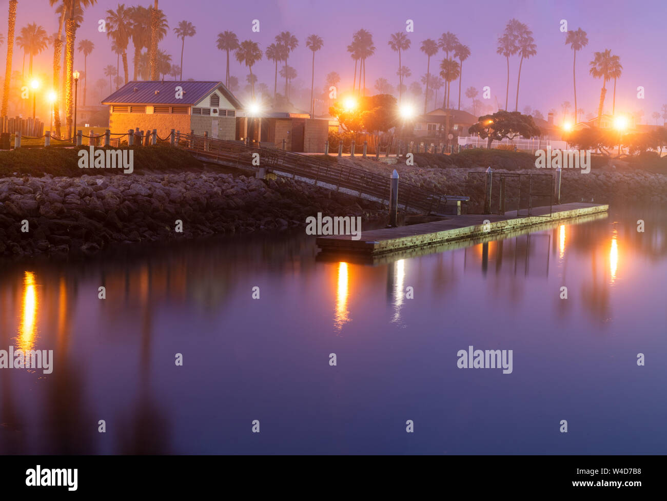 Foggy morning dims the reflecting lights on the smooth surface of the ocean cove dock water. Stock Photo