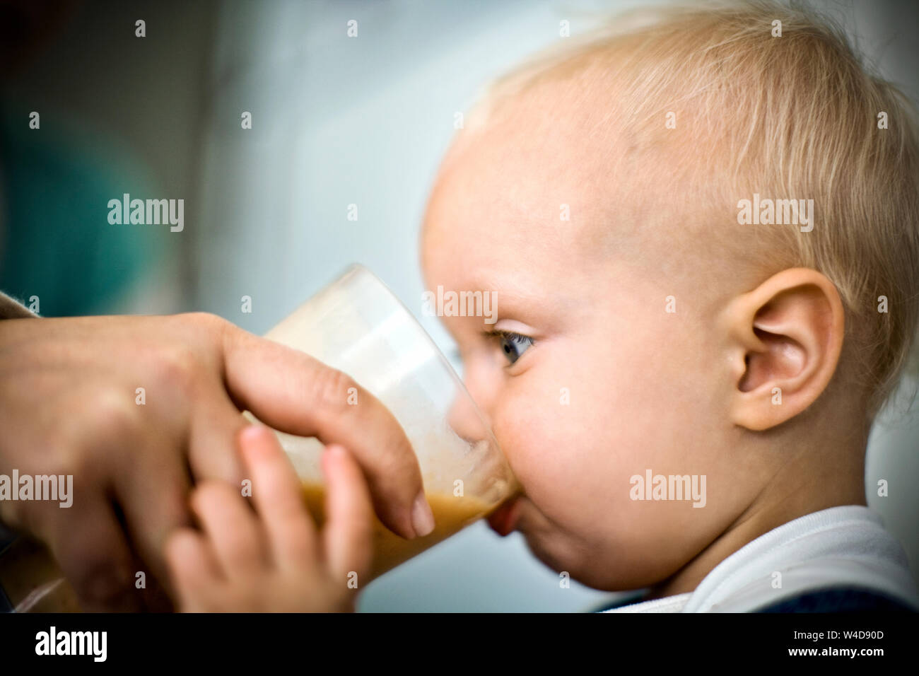 Toddler being helped to drink juice out of a glass. Stock Photo