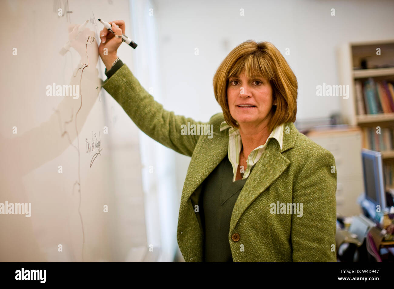 Portrait of a mature female teacher writing on a board standing in a classroom. Stock Photo