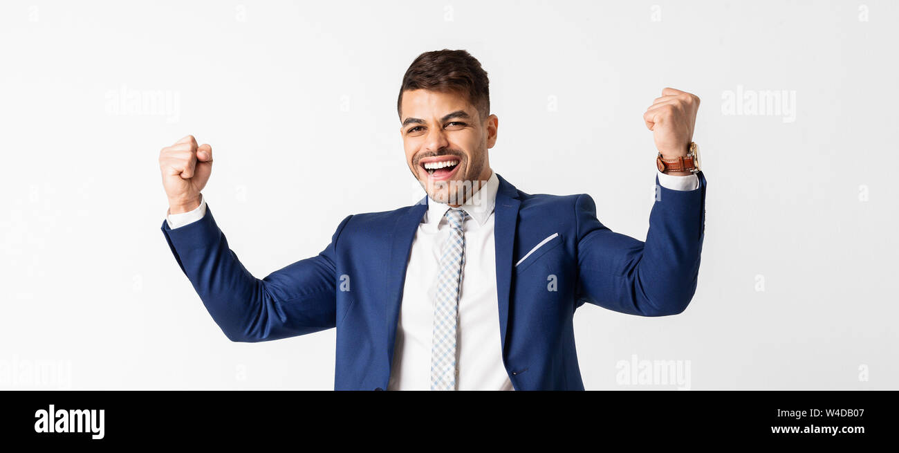 Excited businessman shakes clenched fists on white studio background