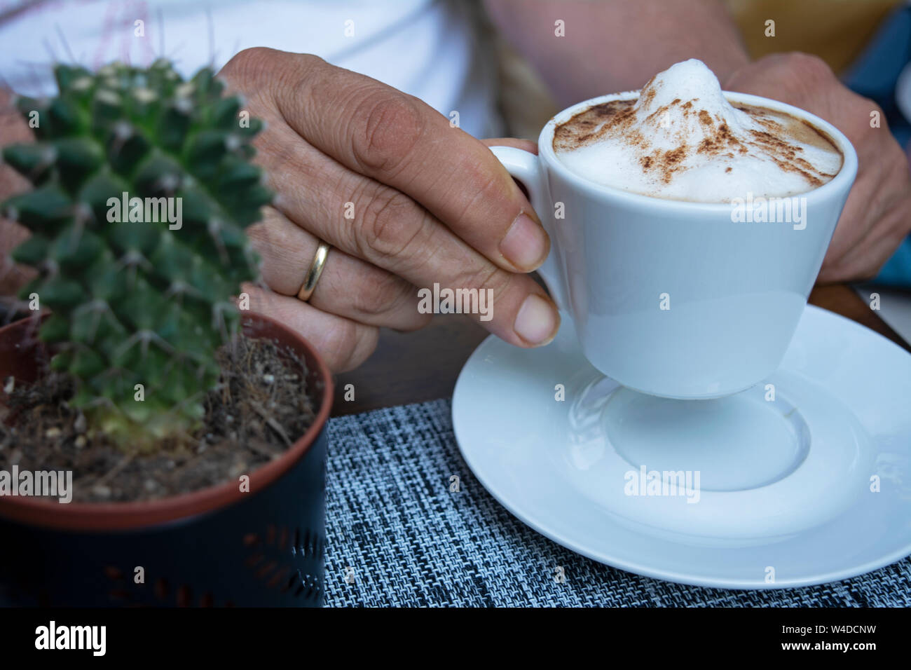 Close up of a man's hand holding a cup of warm cappuccino. At a coffee shop, doing his morning routine. With a wedding ring on his finger. Stock Photo