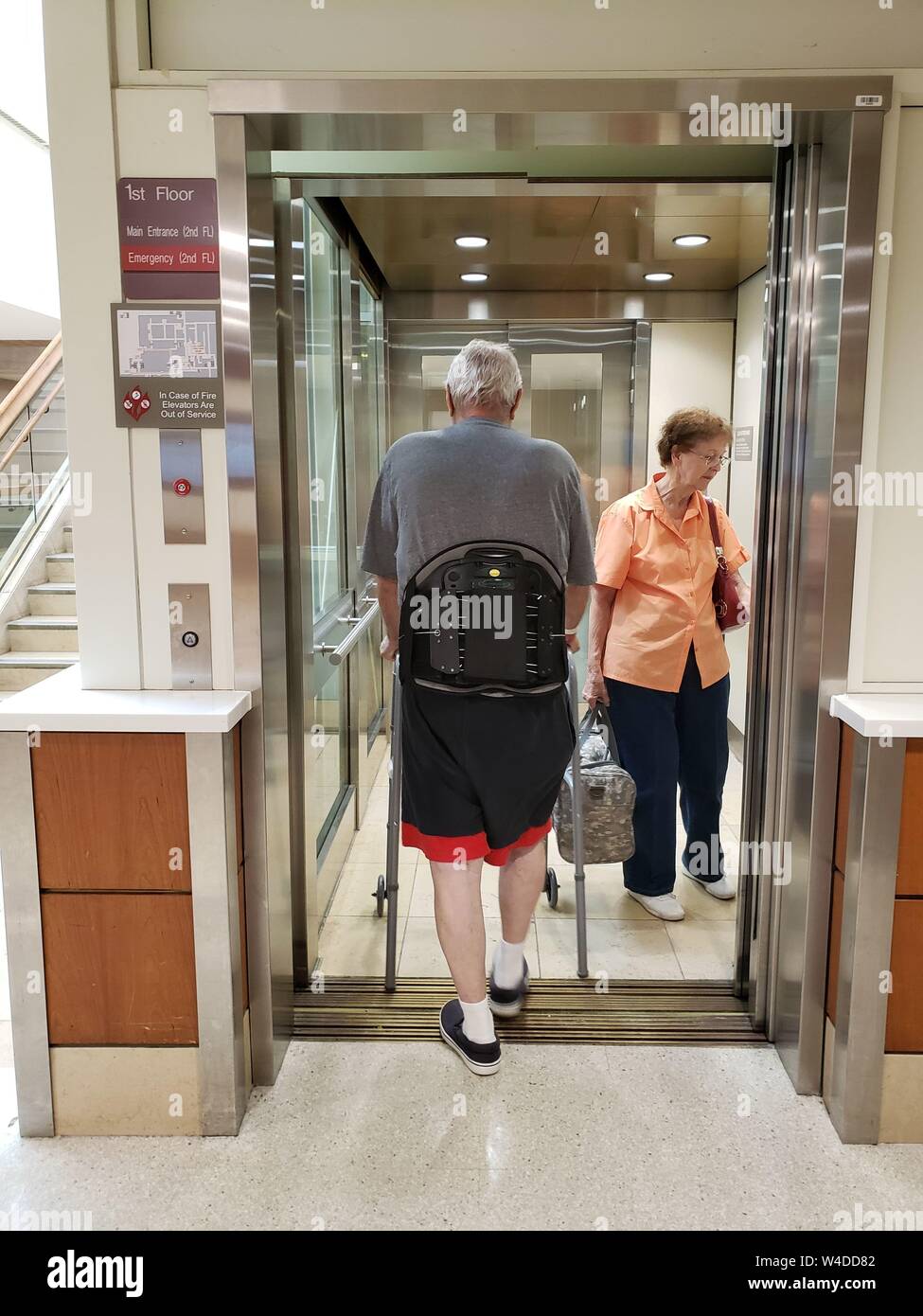 Elderly couple entering hospital elevator to leave hospital following back surgery. Stock Photo