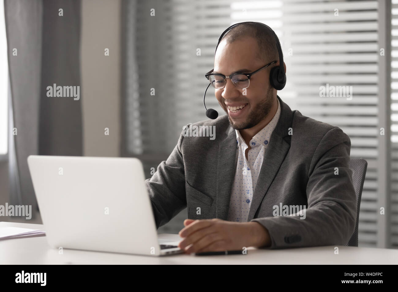 Smiling african man wearing wireless headset video calling on computer Stock Photo