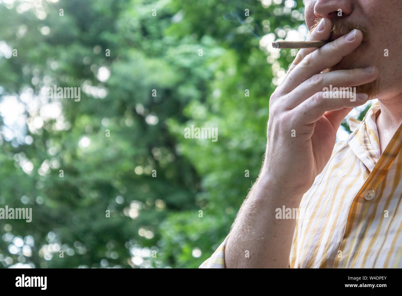 Male working man wearing button down collared shirt holding and smoking marijuana blunt joint for relaxation with blank empty room space for copy or t Stock Photo