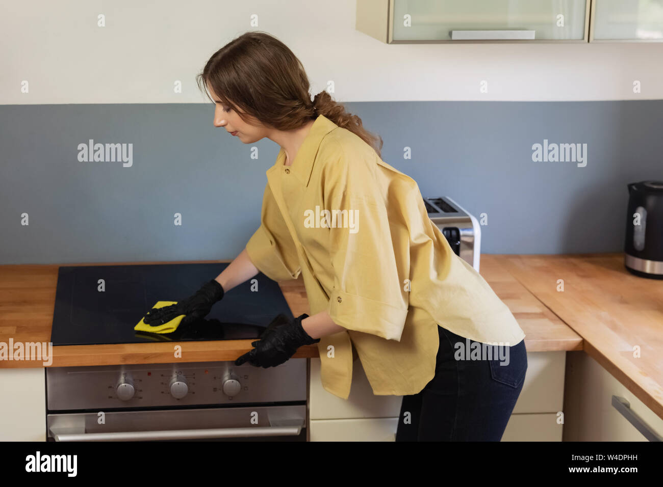 A young woman cleans up in the kitchen, washing dishes. She is tired and not satisfied with the fact that she needs to do it. Stock Photo