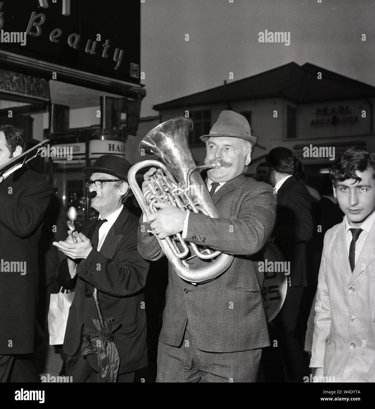 1960s, historical, comedy stars of the radio panel game, 'Does The Team Think'  walking down the street, including Jimmy Edwards, the creator the game, playing a trumbone and one playing the spoons. A British comedy writer and actor, Edwards was famous for his long 'handlebar' moustache. The popular panel game, a parody of 'Any Questions' was played for laughs and ran for nearly twenty years. Stock Photo