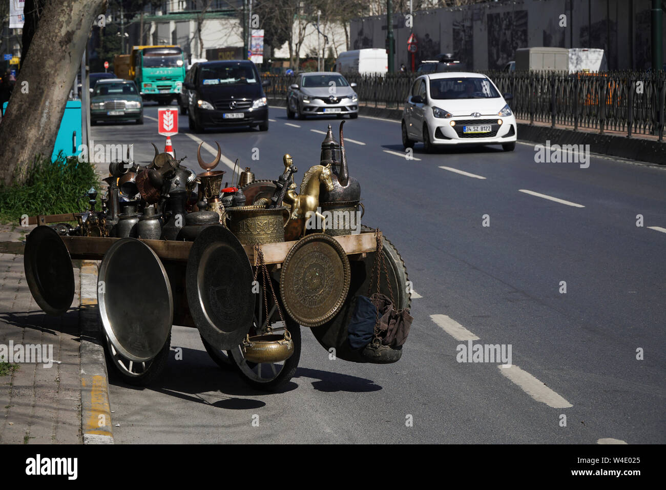 Istanbul, Turkey - April 5, 2018 : There are many antique metal objects on a wheelbarrow at road with vehicles. Like trays, bowls and pitchers. Stock Photo