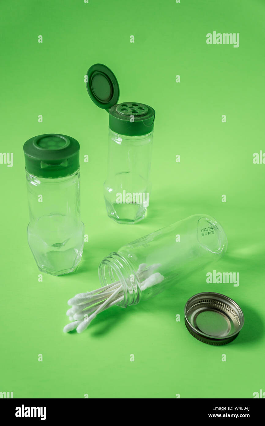 3 Glass spice jars on lime green background with blank empty room space for text or copy. Three kitchen bottles recycled and reused to store cotton sw Stock Photo
