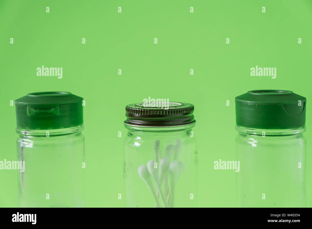 3 Glass spice jars on lime green background with blank empty room space for text or copy. Three kitchen bottles recycled and reused to store cotton sw Stock Photo
