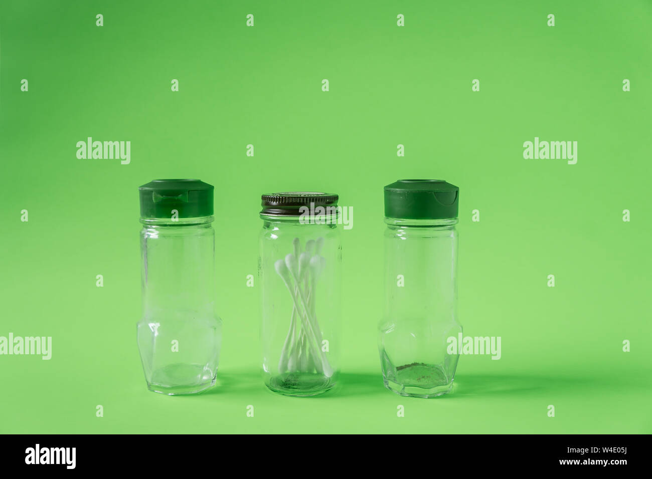 3 Glass spice jars on lime green background with blank empty room space for text or copy. Three kitchen bottles recycled and reused to store cotton sw Stock Photo