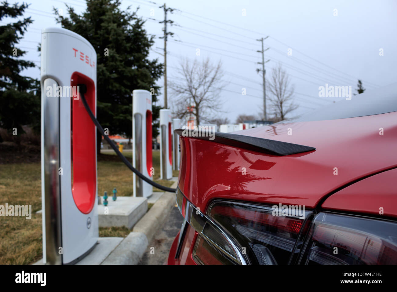Red Tesla Model S charging at Tesla Supercharger as seen with rear carbon fiber spoiler. Stock Photo