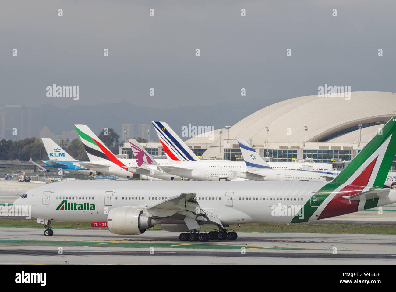 Alitalia Boeing 777 aircraft shown taxiing at LAX. A number of non-American jets are visible in the background. Stock Photo
