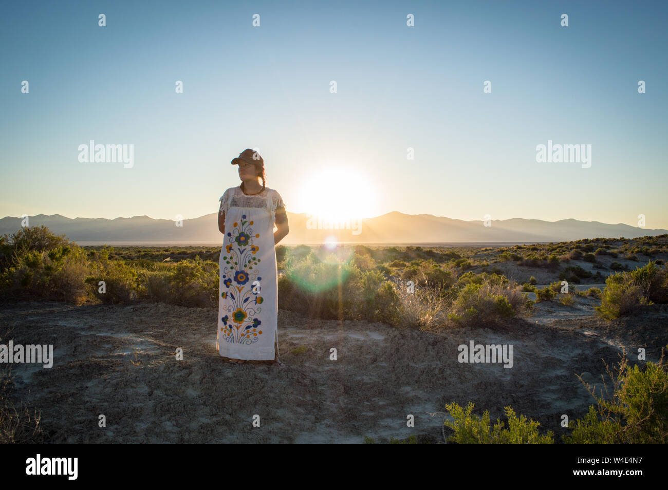 A young woman in an embroidered dress stands in front of a dramatic sunset over the Black Rock Desert. Stock Photo