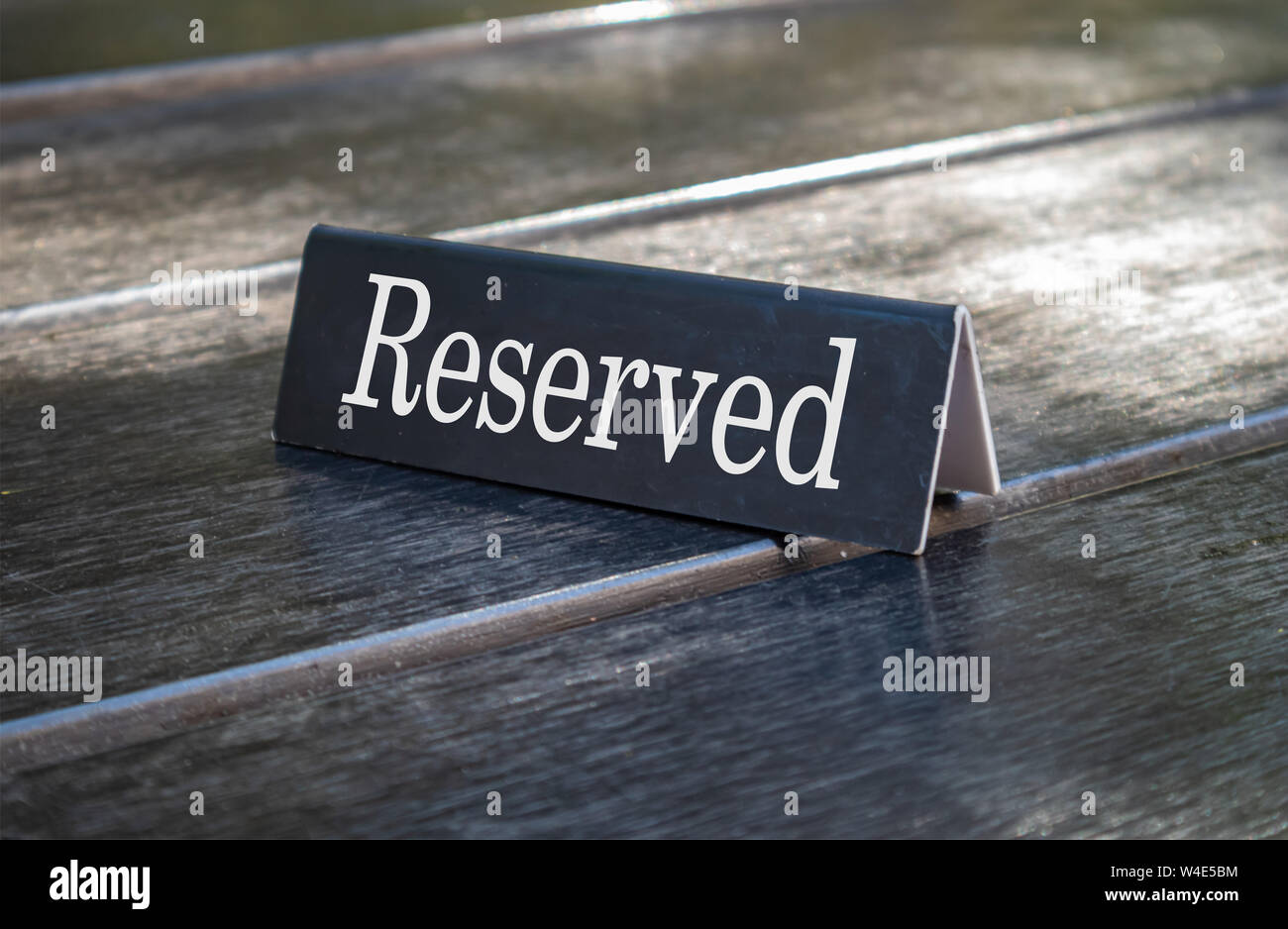 Reserved sign, reservation concept. Text reserved on metal black color plate, white color letters, on wooden table. Close up view with details Stock Photo