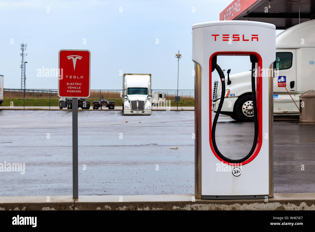 Tesla Supercharger Stall and 'Tesla Electric Vehicle Only' sign with truck-stop in background. Stock Photo