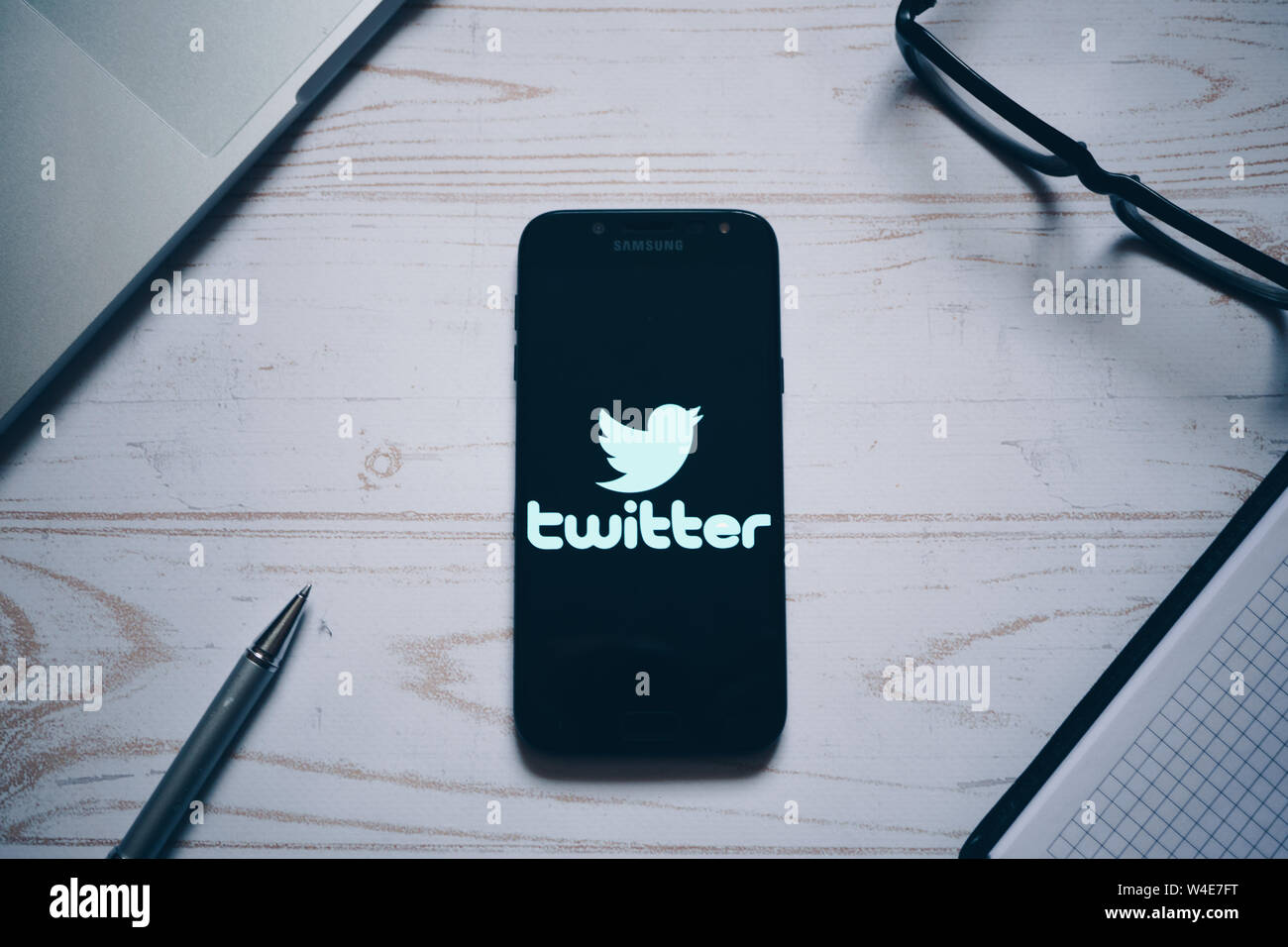 Nizhyn, Ukraine/ July-16-2019: Twitter app logo on the screen of modern smartphone. Flat lay. Laptop, glasses, notebook and pen on background. Social Stock Photo