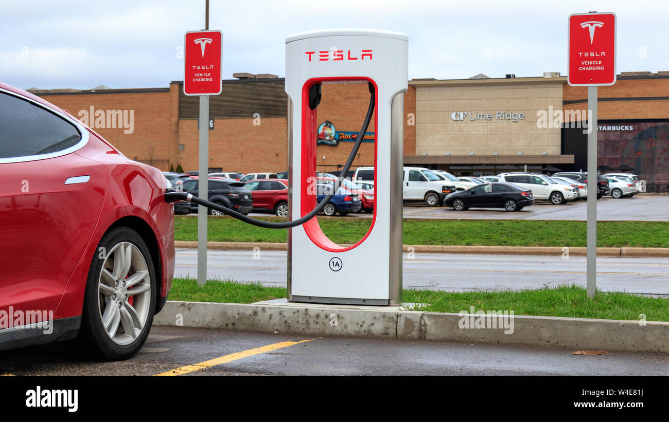 Red Tesla Model S pluggedin to Tesla Supercharger Stall, with Tesla Vehicle Charging sign