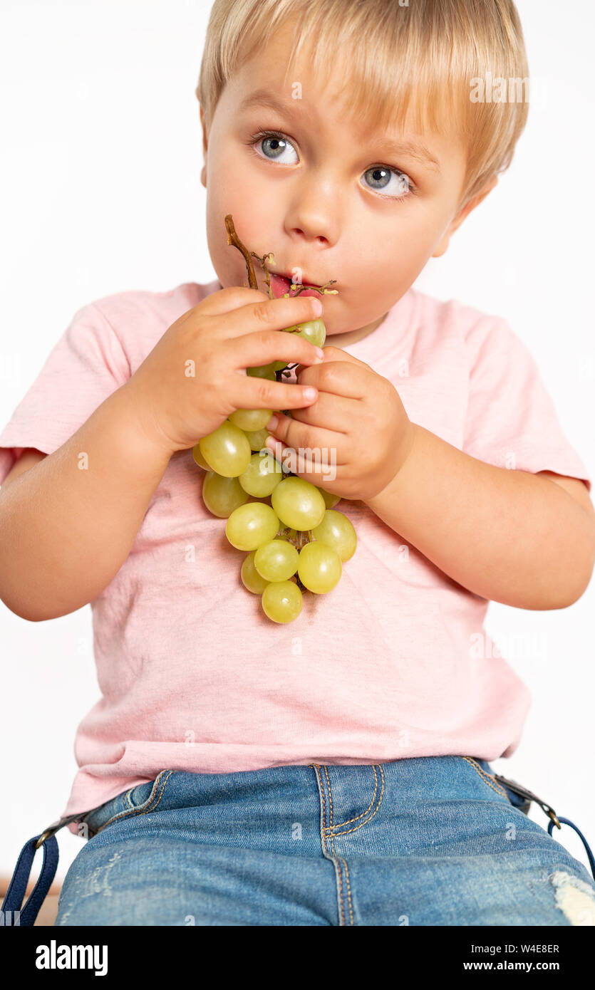Baby boy eating grapes in the studio isolated on white background