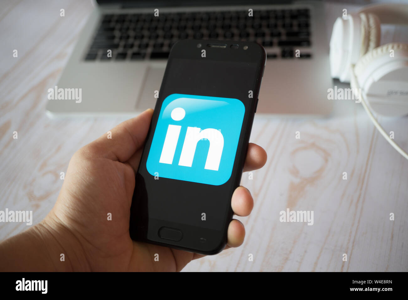 Nizhyn, Ukraine/July-16-2019: Young man in black suite hold smartphone and use Linkedin app. Social media and corporative concept. Stock Photo