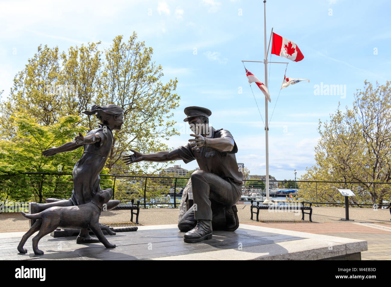 'The Homecoming' Statue, waterfront in downtown Victoria, BC on sunny day with waving Canadian flag in the background. Stock Photo