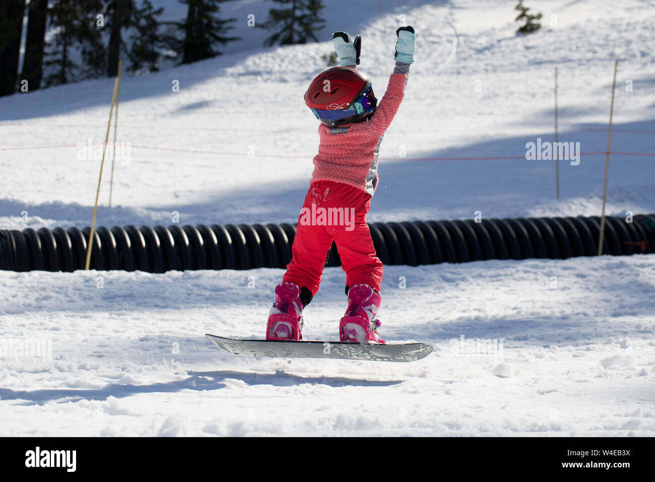 Little Cute Girl Snowboarding making a tricks at ski resort in sunny winter day. Caucasus Mountains. Mount Hood Meadows Oregon Stock Photo