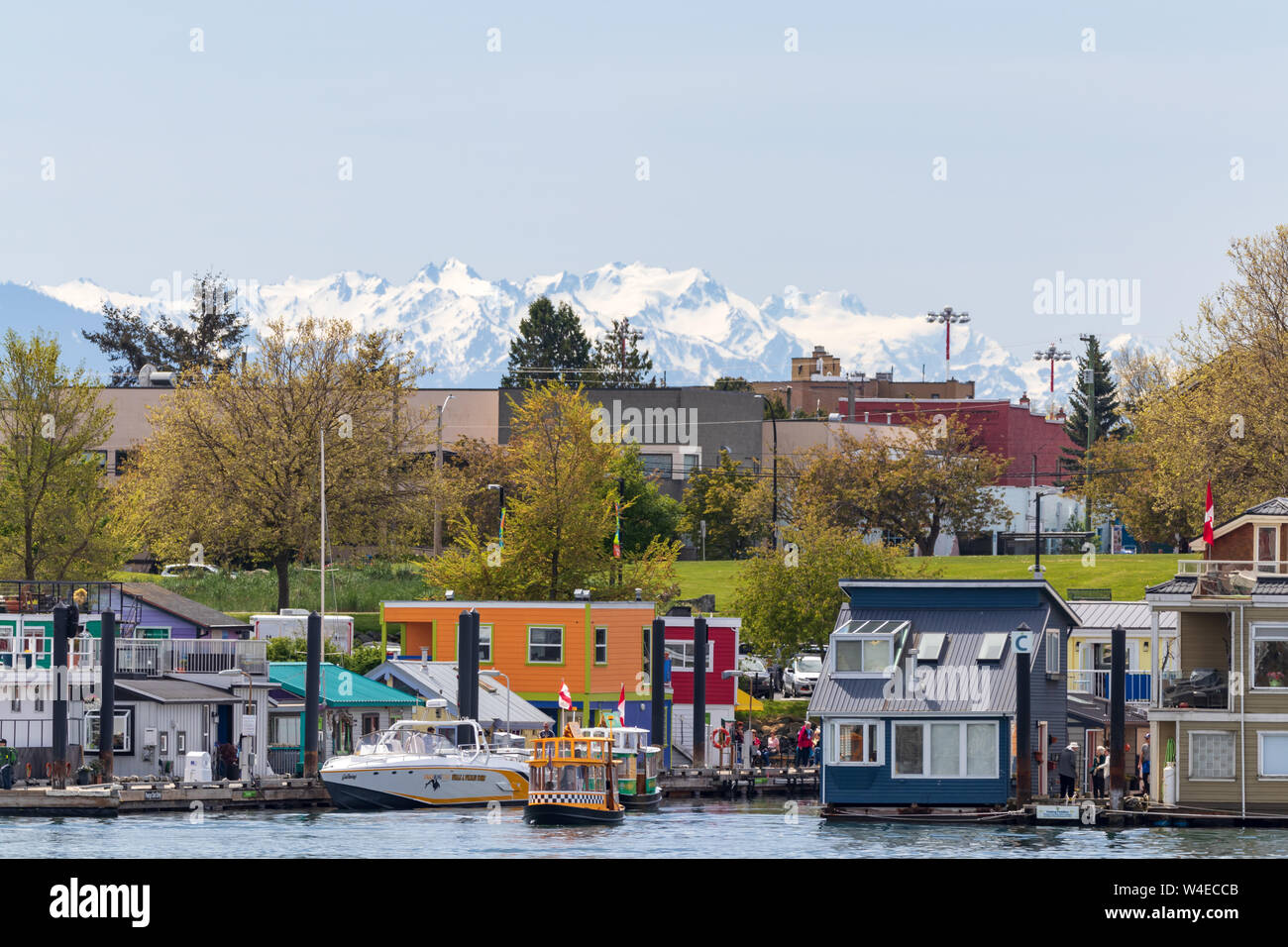 On the water homes/shops and boats in Victoria, BC with snow covered mountains in the background. Stock Photo