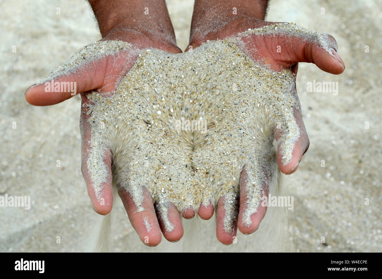 DNA Human A man and woman squatting on Tybee beach have sand pouring through their hands. Stock Photo