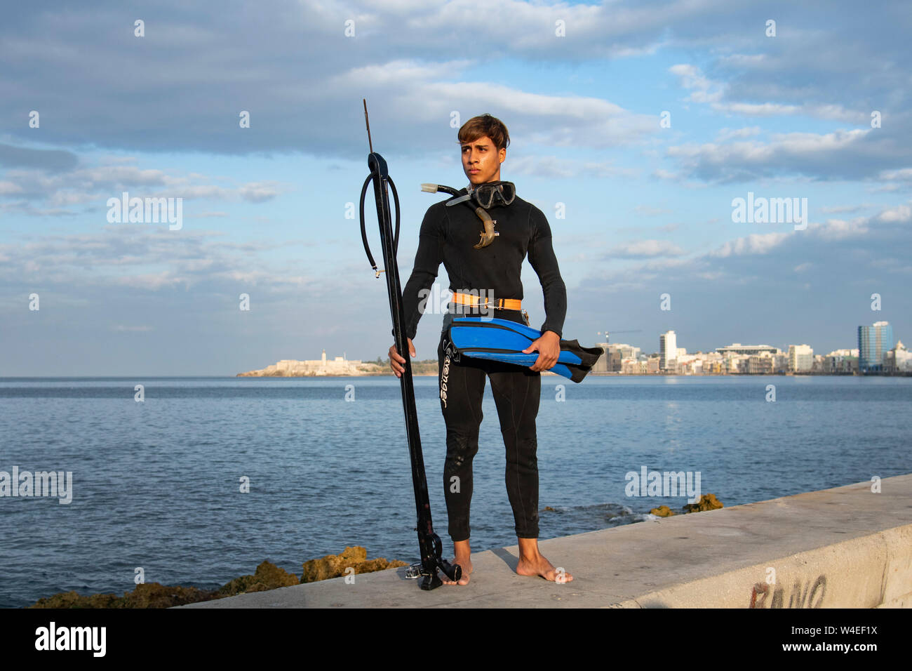 Young Cuban man dressed in his wetsuit poises on Havana's Malecon seawall before going diving into the Caribbean waters below Stock Photo