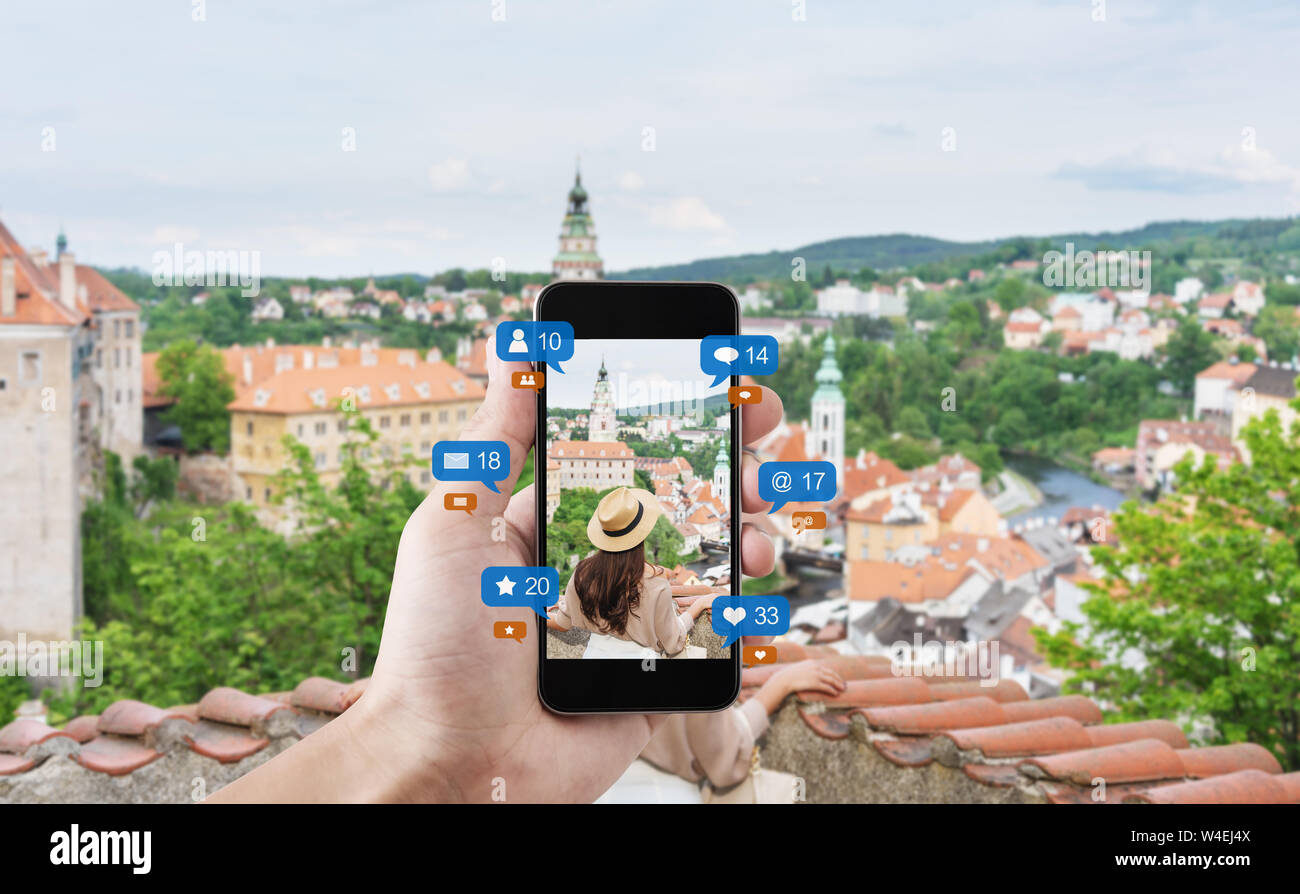 Hand using mobile smart phone taking photo of woman traveling in Cesky krumlov, Czech Republic, with social media and social network notification icon Stock Photo